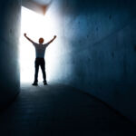 A man standing in the light at the end of a dark tunnel